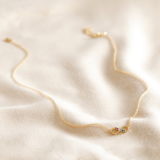 Full Chain of Estella Bartlett Multicoloured Crystal Infinity Pendant Necklace in Gold on Beige Fabric