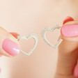Model with pink nails holding the Estella Bartlett Crystal Heart Hoop Earrings in Silver