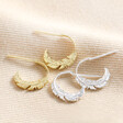 Estella Bartlett Feather Hoop Earrings in Gold with silver version on top of beige coloured fabric