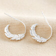 Estella Bartlett Feather Hoop Earrings in Silver on top of beige coloured fabric