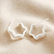 Estella Bartlett Flat Wave Hoop Earrings in Silver on beige fabric