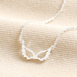Estella Bartlett Angel Wings Pendant Necklace in Silver on top of beige coloured fabric