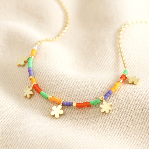 Close Up of Estella Bartlett Ditsy Flower Miyuki Charm Necklace in Gold on Beige Fabric