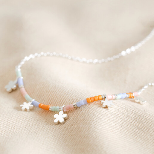 Close Up of Estella Bartlett Ditsy Flower Miyuki Charm Necklace in Silver on Beige Fabric