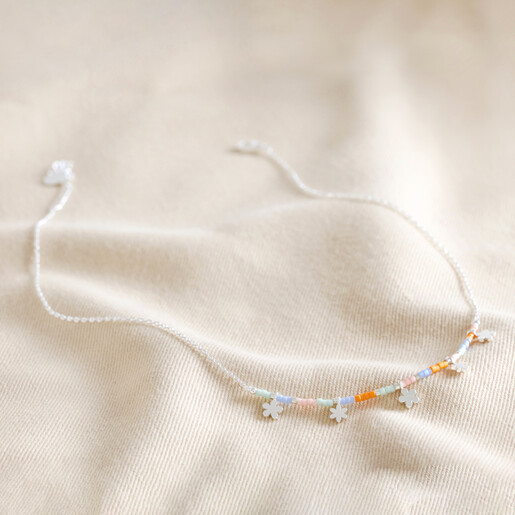 Full Chain of Estella Bartlett Ditsy Flower Miyuki Charm Necklace in Silver on Beige Fabric