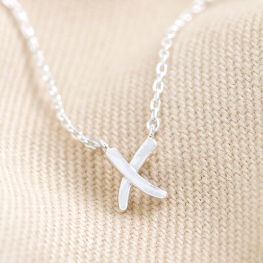 Close Up of Estella Bartlett Kiss Pendant Necklace in Silver on Beige Fabric