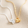 Close Up of Estella Bartlett Knot Pendant Necklaces In Gold and Silver on Beige Fabric