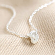 Close Up of Estella Bartlett Knot Pendant Necklace In Silver on Beige Fabric