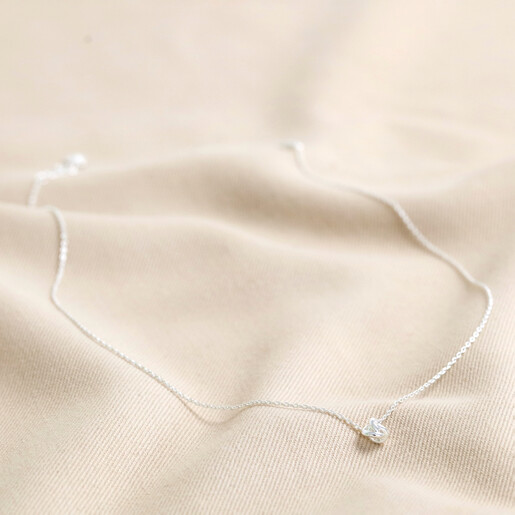 Full Chain of Estella Bartlett Knot Pendant Necklace In Silver on Beige Fabric