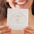 Close Up of Estella Bartlett Pavé Smiley Pendant Necklace Gold in Packaging Held by Model