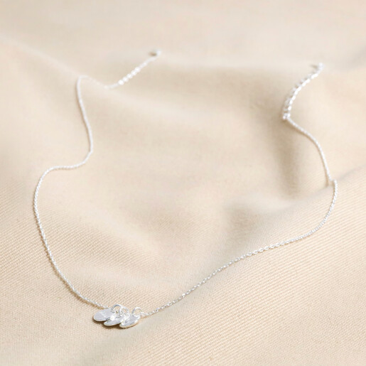 Full Chain of Estella Bartlett Triple Disc Charm Necklace In Silver on Beige Fabric