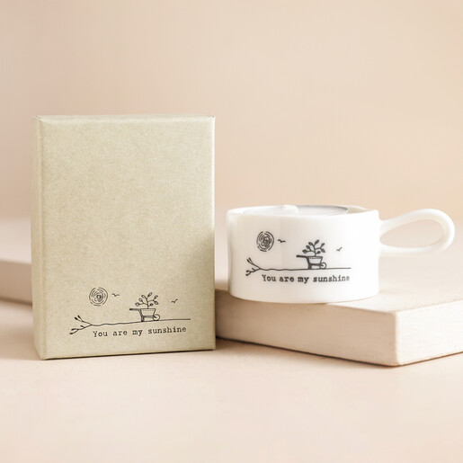 East of India You Are My Sunshine Tealight Holder on top of raised surface with gift box to the side in front of beige backdrop