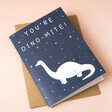 'You're Dino-Mite' Greetings Card with Envelope on Pink Surface
