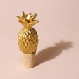 Gold Pineapple Bottle Stopper on Pink Surface