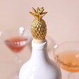 Gold Pineapple Bottle Stopper in White Bottlle with Glasses in the Background