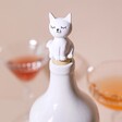 Seated Cat Bottle Stopper in the top of a white bottle with glasses in the background