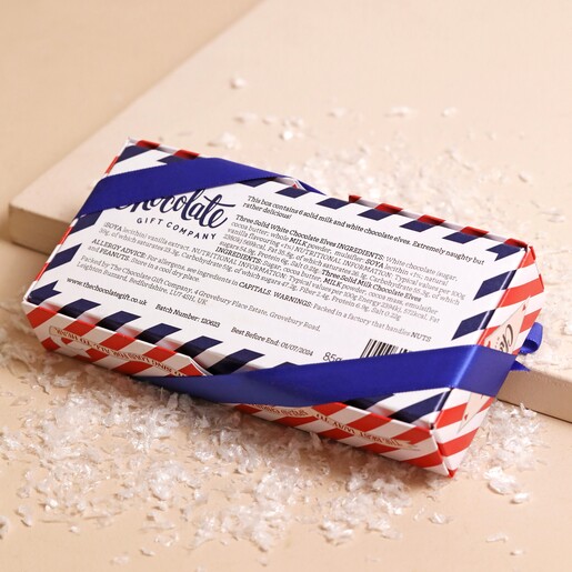 Back of The Chocolate Gift Company Naughty Chocolate Elves Box on top of beige surface with fake snow