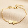 Linked Solid Hearts Charm Bracelet in Gold laid out on neutral coloured fabric