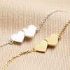 Close up of Linked Solid Hearts Charm Bracelet in Gold next to silver version on top of beige material