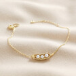Pearl Three Peas in a Pod Charm Bracelet in Gold on neutral coloured fabric