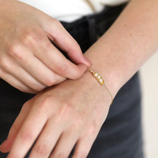 Close up of Pearl Three Peas in a Pod Charm Bracelet in Gold on model holding chain between fingers