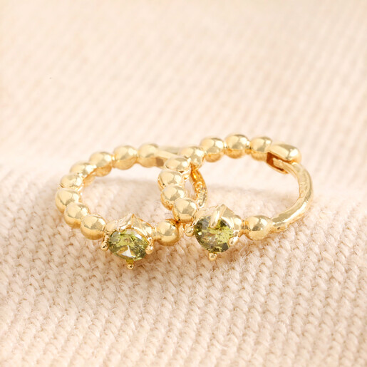 August Birthstone Huggie Hoop Earrings in Gold on top of beige coloured fabric 