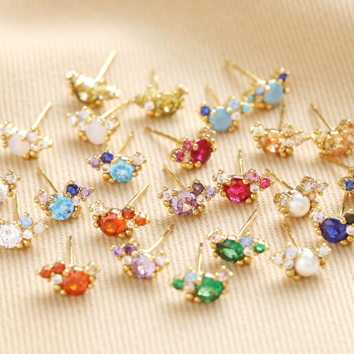 Birthstone Cluster Stud Earrings in Gold Birthstone Cluster Stud Earrings in Gold laid out on beige fabric