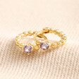 February Birthstone Huggie Hoop Earrings in Gold laid out on top of beige fabric