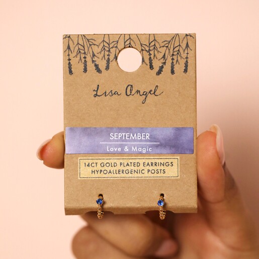 Model holding Birthstone Huggie Hoop Earrings in Gold in packaging against wall