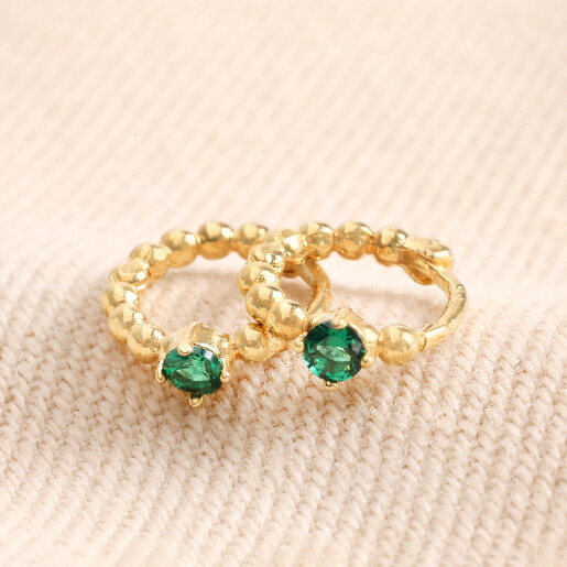 May Birthstone Huggie Hoop Earrings in Gold laid out on top of beige fabric