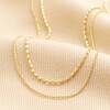 Close up of Double Ball Chain Necklace in Gold on beige Fabric