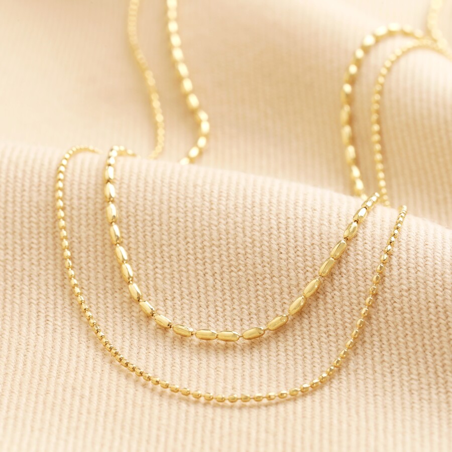 Double Ball Chain Necklace in Gold arranged on top of beige material
