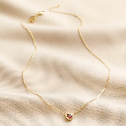 Red Stone Heart Pendant Necklace in Gold full length against neutral coloured fabric