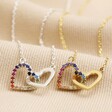 Interlocking Rainbow Crystal Hearts Necklace in Silver next to gold on top of beige coloured fabric