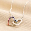 Interlocking Rainbow Crystal Hearts Necklace in Silver on top of beige coloured fabric