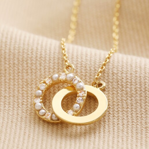 Close up of Interlocking Pearl and Crystal Hoops Necklace in Gold laid on top of neutral fabric