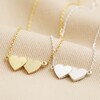 Linked Hearts Pendant Necklace in Gold with Silver Version Next to it on Beige Fabric