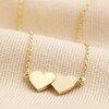 Close Up of Linked Hearts Pendant Necklace in Gold on Beige Fabric 