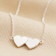 Close Up of Linked Hearts Pendant Necklace in Silver on Beige Fabric