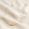 Full Chain of Pearl Three Peas in a Pod Pendant Necklace in Gold on Beige Fabric