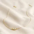 Full Chain of Pearl Three Peas in a Pod Pendant Necklace in Gold on Beige Fabric