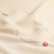 Pink Enamel Daisy Pendant Necklace in Silver laid out over beige coloured fabric