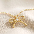Close Up of Tiny Pearl Bow Pendant Necklace in Gold on Cream Background
