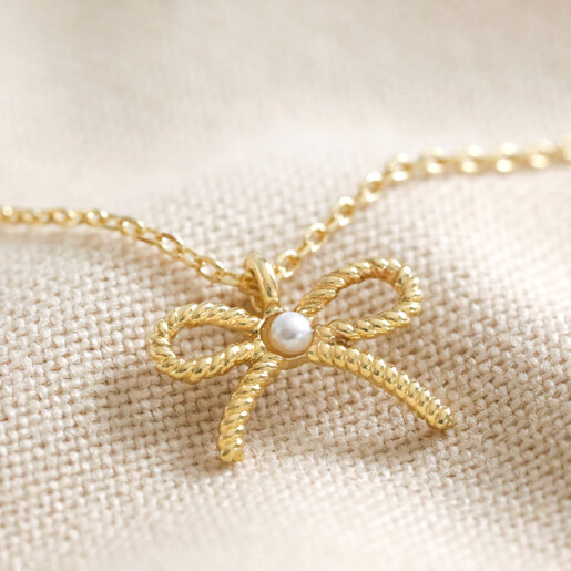 Tiny Pearl Bow Pendant Necklace in Gold Close Up of Tiny Pearl Bow Pendant Necklace in Gold on Cream Background