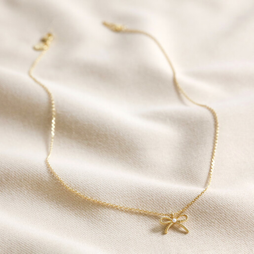 Full Necklace Tiny Pearl Bow Pendant Necklace in Gold on Cream Background