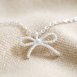 Close Up of Tiny Pearl Bow Pendant Necklace in Silver on Cream Background