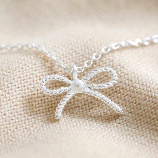 Tiny Pearl Bow Pendant Necklace in Silver Close Up of Tiny Pearl Bow Pendant Necklace in Silver on Cream Background