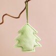 Plush Green Christmas Tree Hanging Decoration hanging from branch in front of pink background