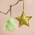 Plush Green Star Hanging Decoration and Christmas tree decoration hanging from branch in front of pink background