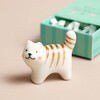 Ceramic cat token standing outside of the Tiny Matchbox Ceramic Cat Token packaging